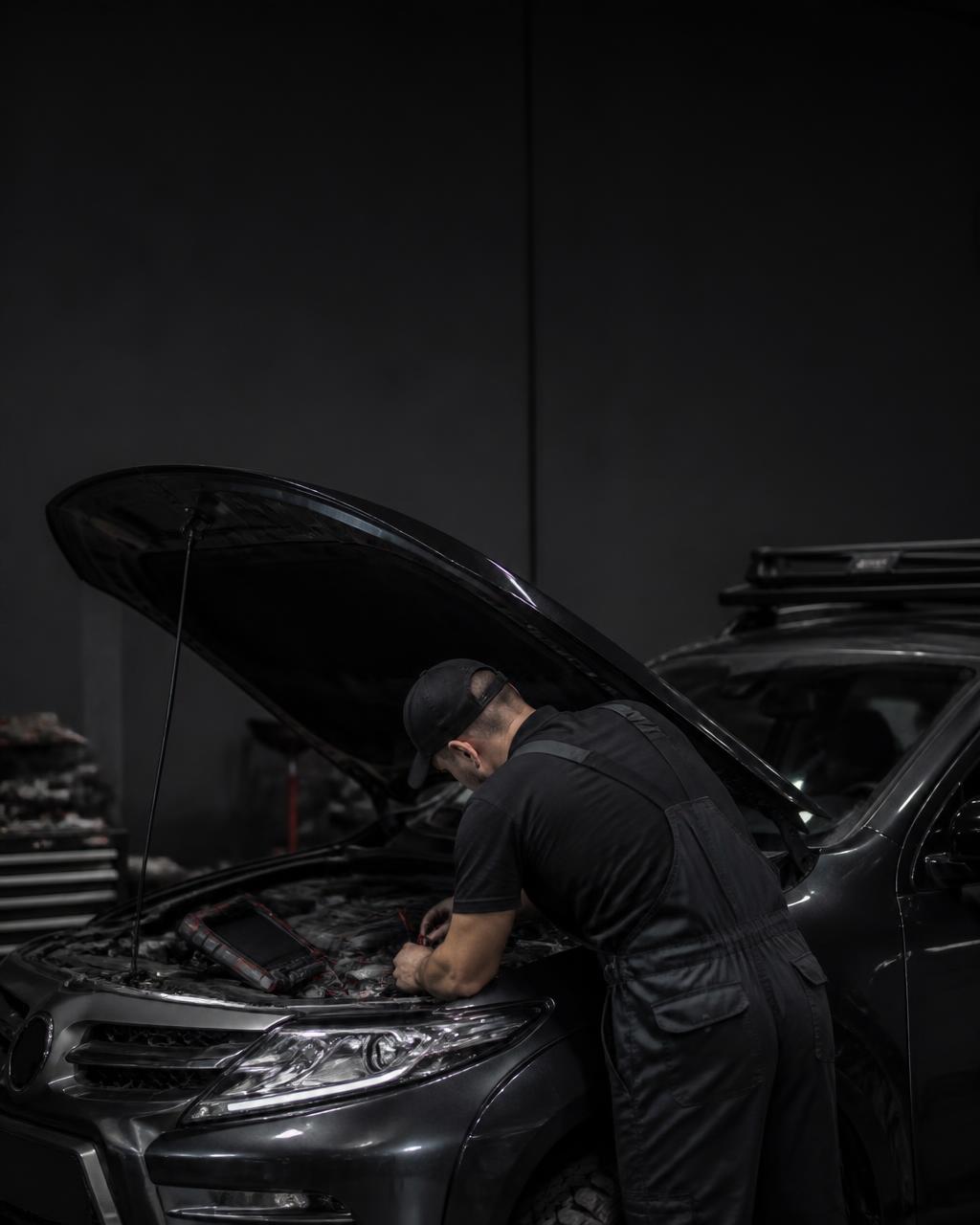 Auto electrician working on a vehicle's wiring loom with a diagnostic scan tool in a workshop